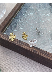 Detailed close-up of matte silver and gold gardenia flower earrings on a vintage tray