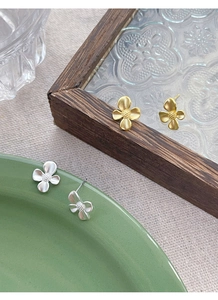 Detailed macro of gold and silver gardenia stud earrings with matte metal texture