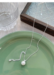 Detail of S925 silver pearl necklace with round beads on a green ceramic plate