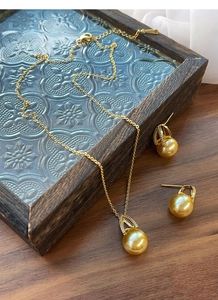 Detail view of gold-plated S925 silver necklace and pearl earrings set on vintage tray
