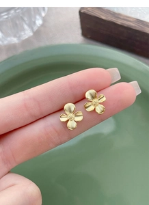 Detailed macro view of matte gold gardenia flower earrings held for scale and texture