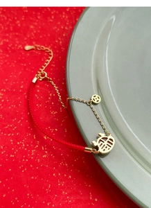 Détail du bracelet en corde rouge et chaîne dorée avec signe Fu ajouré et pièce