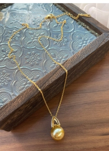 Macro detail of a S925 silver gold pearl pendant with zircon triangle clasp on a wooden tray