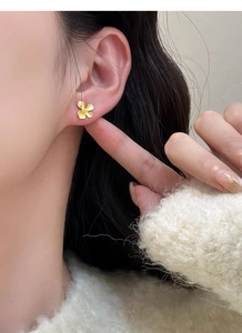 Detail view of a matte gold gardenia stud earring worn by a model in a close-up shot