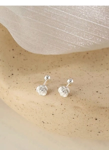 Macro shot of silver camellia earrings with screw-back design on elegant beige tray