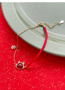 Détail du bracelet en cordon rouge et chaîne dorée avec breloque cœur et fermoir réglable