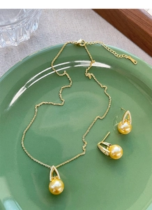 Detailed set of gold pearl necklace and earrings on elegant green ceramic tray
