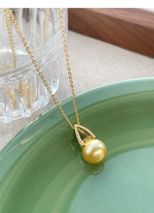 Detail of a golden pearl pendant featuring a geometric diamond-set clasp on a gold chain