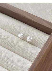 Detail view of S925 sterling silver camellia stud earrings on elegant linen display tray