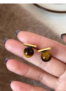 Detailed shot of S925 silver gold bar earrings with tiger eye stone held by hand