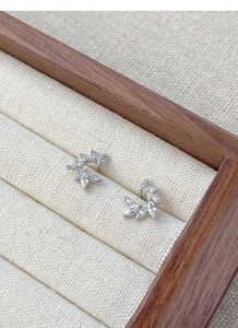 Detail of leaf-shaped silver stud earrings with marquise zircons in a wooden jewelry box