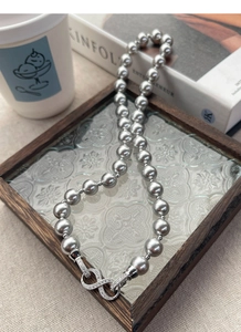 Detail of grey pearl necklace with infinity clasp on a vintage glass tray