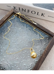 Detailed close-up of a golden pearl pendant necklace on a vintage KINFOLK aesthetic background