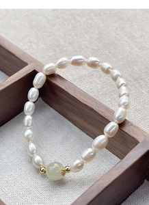 Detailed shot of white freshwater pearls with green jade bead on dark wood tray