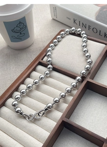 Detailed view of grey pearl necklace featuring a diamond-studded infinity clasp on a soft stand