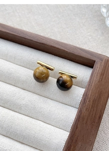 Macro shot of tiger eye stone earrings with gold bars on a cream fabric jewelry tray