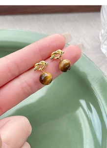 Macro view of gold knot stud earrings with tiger eye stone drop on a ceramic plate