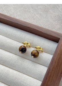 Detailed close-up of S925 silver knot earrings with spherical tiger eye stones in gold finish