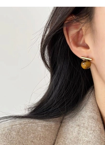 Detailed close-up of a gold geometric stud earring with a brown tiger eye stone on a model