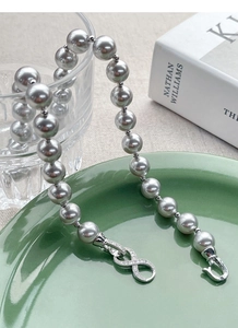 Macro view of grey pearl necklace featuring a sparkling infinity clasp on silk-like surface