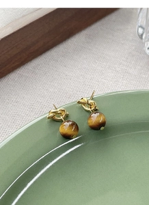Close-up of S925 silver tiger eye stud earrings with gold knot detail on green ceramic