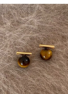 Macro shot of tiger eye stone earrings with golden metal post on soft plush surface