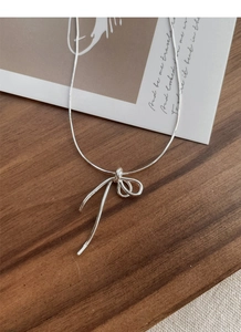 Detail of S925 sterling silver bow necklace displayed on an aesthetic wooden tray