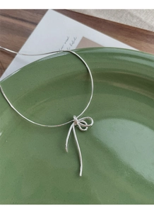 Detail of silver S925 bow-shaped knot pendant resting on a dark green ceramic plate