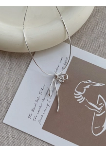 Detailed shot of S925 silver knotted bow pendant with sleek snake chain on a prop card