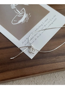 Detail of S925 sterling silver bow knot necklace on rustic wooden surface with linen fabric