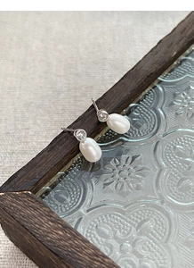 Détail de boucles d'oreilles en argent S925, perles d'eau douce et diamants sur cadre boisé