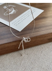 Detail of S925 sterling silver knotted bow necklace on a textured cream fabric background