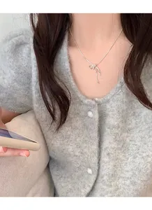 Detail of S925 silver knot bow necklace worn on a grey cardigan for a delicate look