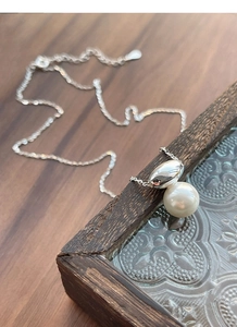 Macro detail of minimalist pearl pendant on a fine silver chain with polished bead accent