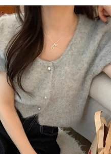 Close-up of golden ribbon bow pendant and soft grey mohair cardigan with pearl buttons