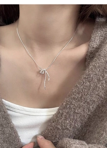 Detail of S925 silver bow pendant necklace worn on a model with a brown sweater