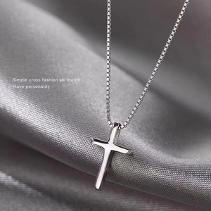 Gros plan d'un collier croix en argent S925 poli avec chaîne gourmette sur soie grise