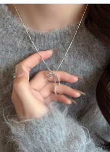 Macro view of a silver ribbon bow pendant necklace worn on a grey knitted sweater
