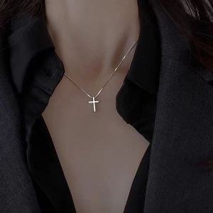 Collier croix minimaliste en argent S925 porté sur un blazer gris foncé et une chemise noire