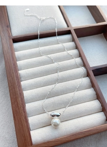 Macro shot of S925 silver necklace with white pearl and oval metal pendant on a tray