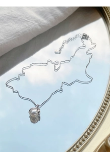 Macro shot of an S925 silver pearl necklace reflecting on a mirror with a blue sky