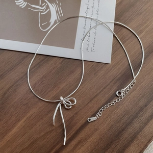 Minimalist S925 sterling silver bow knot necklace on a warm vintage wooden background