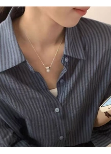 Detailed close-up of a single white pearl pendant with golden chain worn on a model