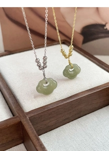 Détail de colliers S925 en argent et or avec pendentifs en jade vert sur support en bois
