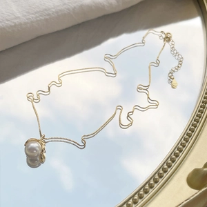 Elegant S925 silver pearl necklace with a gold leaf clasp on a reflective mirror base