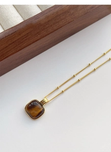 Macro shot of square tiger eye pendant on a gold bead chain with a wooden jewelry box