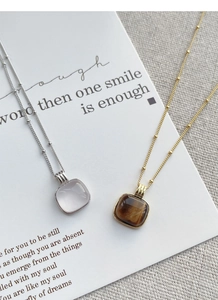Detailed shot of silver pink quartz and gold tiger eye square pendants on bead chains