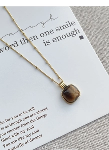Detailed close-up of a square tiger eye stone pendant on a gold beaded chain necklace