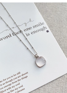Detail of square pink quartz pendant with minimalist silver beaded chain on fabric