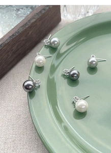 Close-up of S925 silver pearl earrings in white and gray colors on green ceramic plate